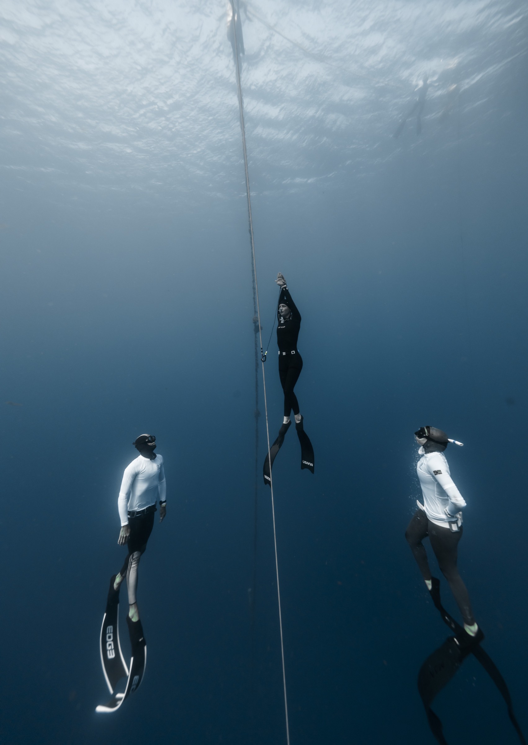 Natalie Bruce ascending the line between two safety divers in deep blue open water